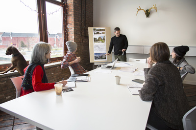 Designer using color printer, copier, and scanner in shared workspace.